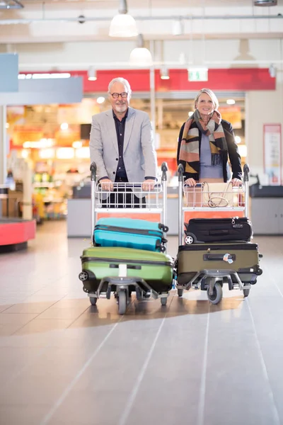 Pareja de negocios senior feliz con equipaje en carritos en el aeropuerto —  Fotos de Stock