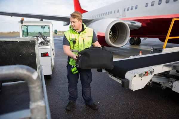 Рабочий поднимает багаж с конвейера, прикрепленного к самолету — стоковое фото