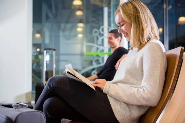 Seitenansicht einer lächelnden Frau, die am Flughafen Buch liest — Stockfoto