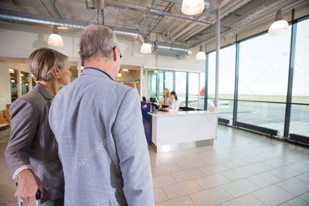 Business Couple Looking At Receptionists Working In Airport