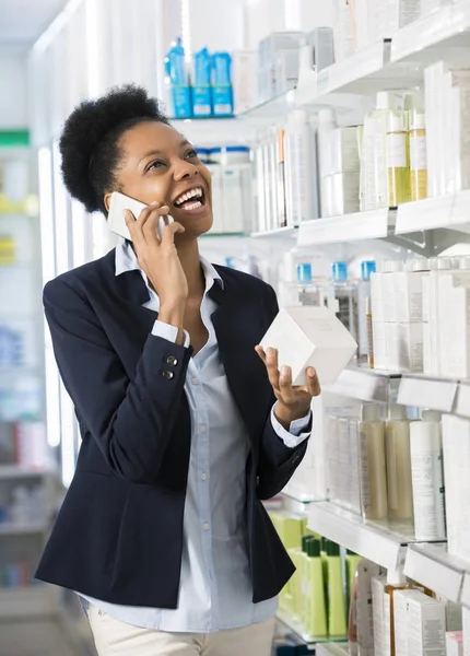 Frau hält Produkt in der Hand, während sie auf dem Handy kommuniziert — Stockfoto