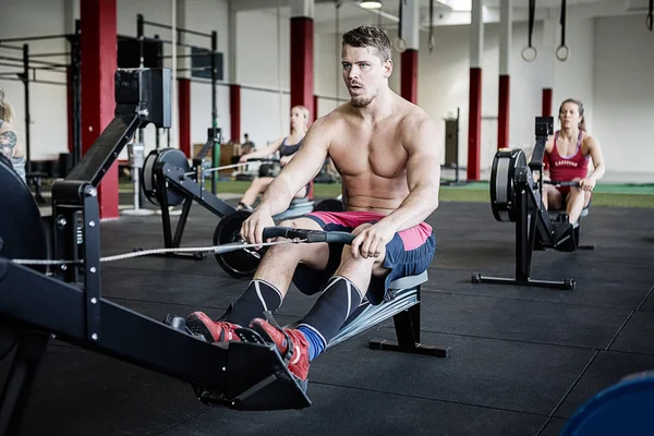 Hombre sin camisa usando la máquina de remo en el gimnasio — Foto de Stock