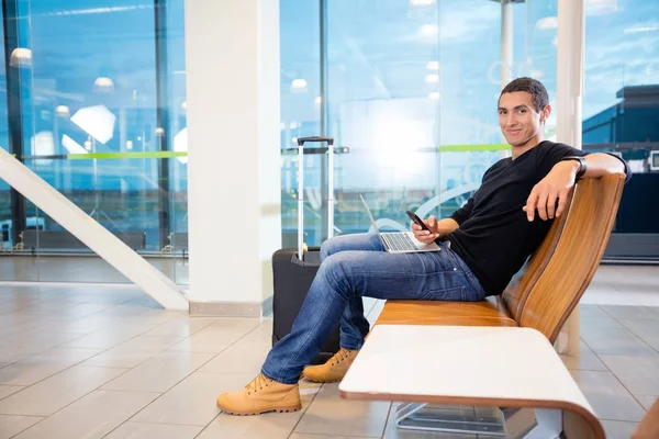 Jovem com telefone celular e laptop no aeroporto — Fotografia de Stock