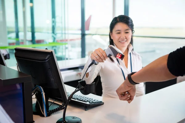 Recepcionista sonriente escaneando reloj inteligente de pasajeros en el aeropuerto —  Fotos de Stock