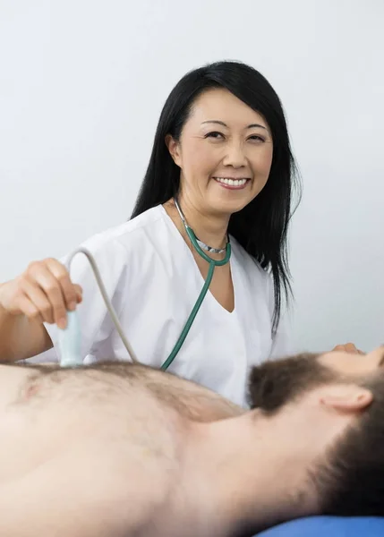 Feliz médico realizando una prueba de ultrasonido en el paciente —  Fotos de Stock