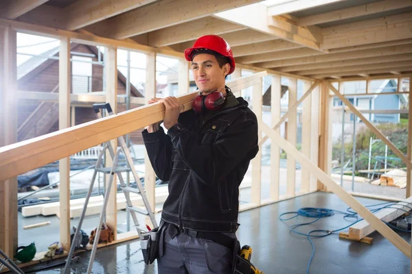 Carpintero joven que lleva madera en el sitio de construcción — Foto de Stock