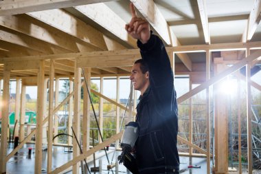 İnşaat alanında işaret ederken matkap tutan bir marangoz