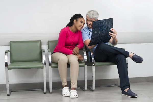 Médico y paciente mirando rayos X mientras está sentado en sillas —  Fotos de Stock