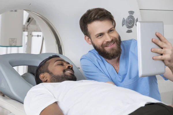 Radiologista mostrando o comprimido digital ao paciente que jaz na tomografia computadorizada — Fotografia de Stock