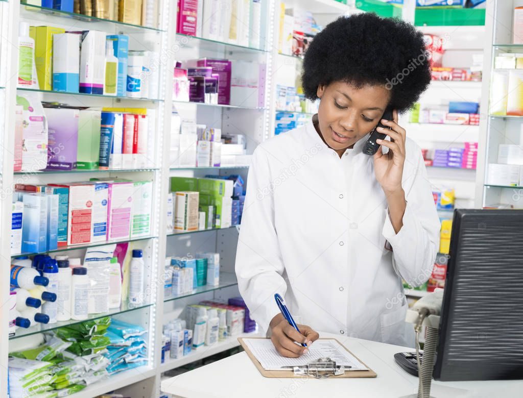 Chemist Writing On Clipboard While Using Cordless Phone