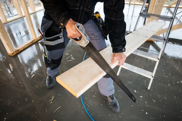 Baixa seção de carpinteiro usando serra de mão para cortar prancha — Fotografia de Stock