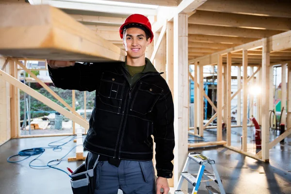 Carpintero macho sonriente que lleva madera en el sitio de construcción —  Fotos de Stock