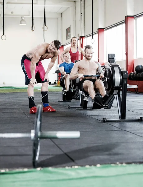 Man Standing By Friends Exercising On Rowing Machine — Stock Photo, Image