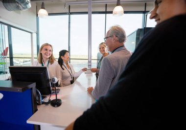 Gülümseyen personel yolcu havaalanında kontuarında bakarak