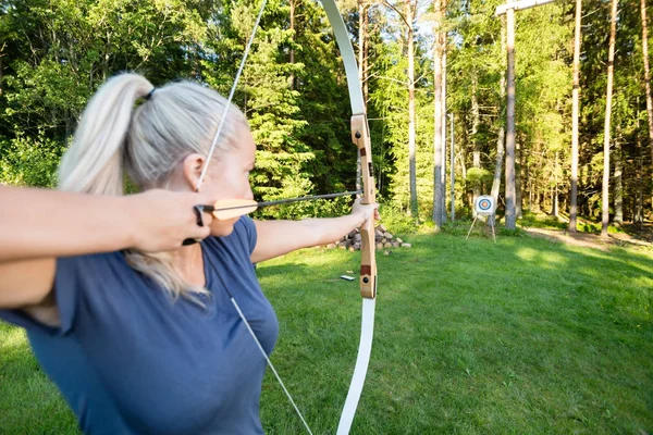 Atleta feminina apontando seta para alvo bordo na floresta — Fotografia de Stock