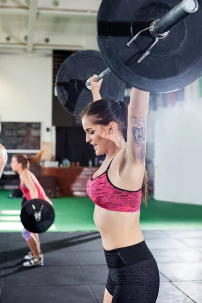 Passar unga kvinnliga lyfta skivstång i gymmet — Stockfoto