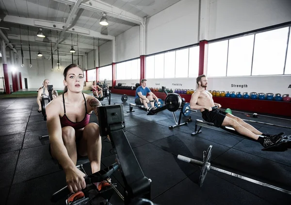 Atleta usando máquina de remo con amigos en el gimnasio — Foto de Stock