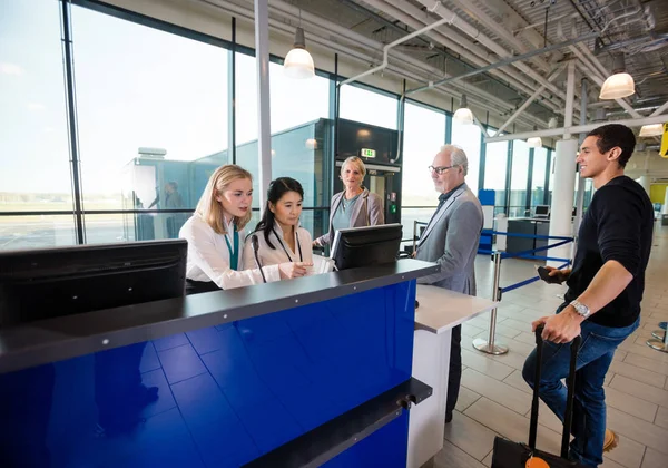Funcionários usando o computador enquanto os passageiros esperam no aeroporto — Fotografia de Stock