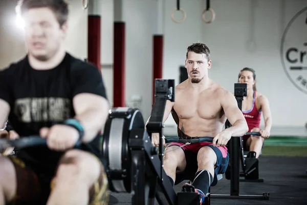 Homme musculaire s'exerçant sur la machine à ramer dans le gymnase Image En Vente