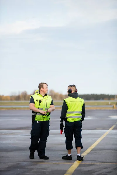 Arbeiter in reflektierenden Jacken stehen auf der Landebahn des Flughafens lizenzfreie Stockfotos