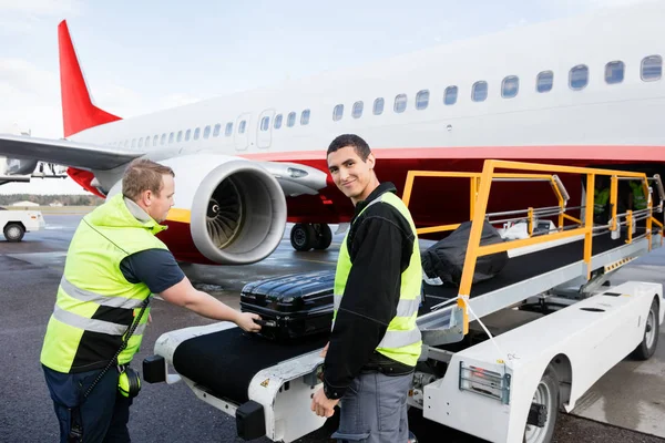 Worker Smiling While Colleague Unloading Luggage On Runway Stock Picture