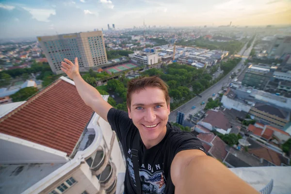 Un giovane uomo coraggioso, che fa un selfie sul bordo del tetto del grattacielo. Surabaya, Indonesia — Foto Stock