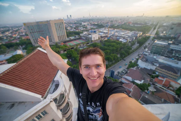 Genç bir adam, bir selfie gökdelenin çatı kenarında yapım cesur. Surabaya, Endonezya