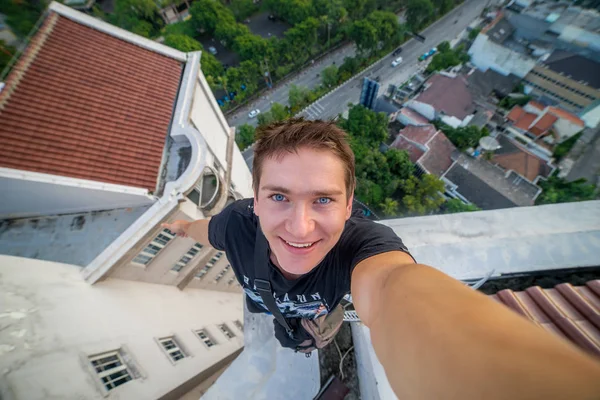 Genç bir adam, bir selfie gökdelenin çatı kenarında yapım cesur. Surabaya, Endonezya