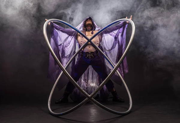 Personaje asesino de cuento de hadas en una capa púrpura con una capucha con dos grandes aros de rueda de cyr — Foto de Stock