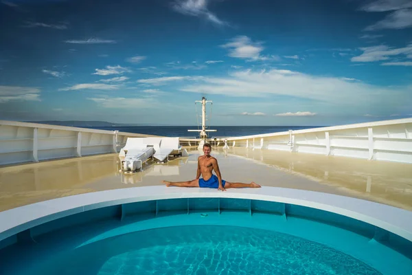 Молодий м'язистий хлопець сидить на розколі на басейнах на носі круїзного корабля на тлі моря — стокове фото