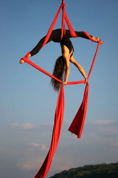 Bella e flessibile artista del circo femminile che balla con seta aerea su sfondo cielo — Foto Stock