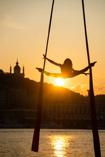 Silueta de una mujer acróbata flexible sobre seda aérea durante una puesta de sol en el fondo de la ciudad de Kiev. concepto de libertad y paz — Foto de Stock