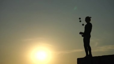 Sirk sanatçısı renkli günbatımında toplarıyla hokkabazlık yapıyor.