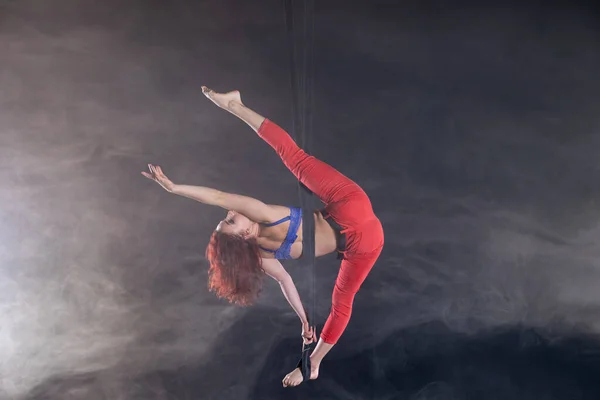 Mujer atlética, sexy y flexible artista de circo aéreo con pelirroja en correas aéreas sobre fondo negro — Foto de Stock