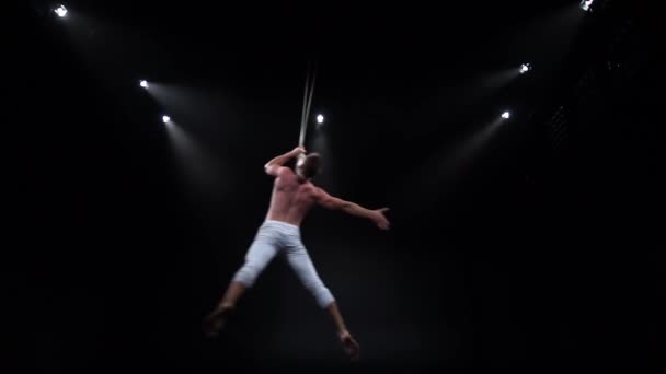Мужчина мускулистый циркач на воздушных ремнях делает сильные трюки в воздухе на черном фоне — стоковое видео