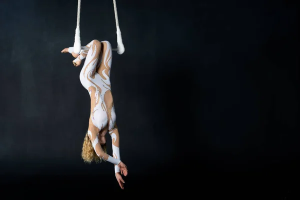 Uma jovem executa os elementos acrobáticos no trapézio aéreo. Estúdio de filmagem performances em um fundo preto — Fotografia de Stock