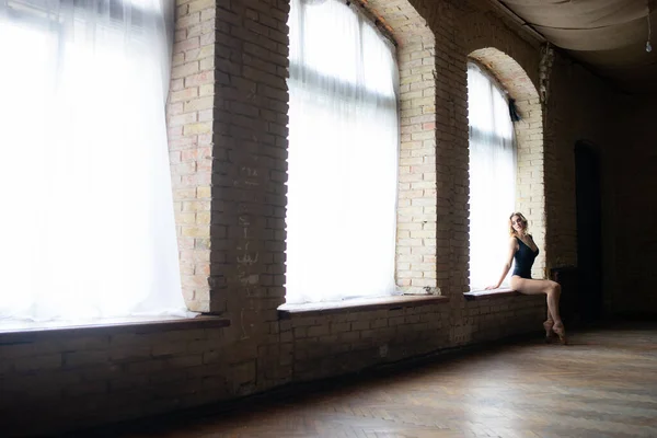 Silhouette einer jungen, flexiblen, wohlgeformten Ballerina, die auf dem riesigen Fenster sitzt. Konzept von Einsamkeit und Traurigkeit — Stockfoto