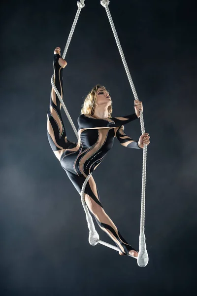 Ein junges Mädchen führt die akrobatischen Elemente am Lufttrapez vor. Studioaufnahmen auf schwarzem Hintergrund — Stockfoto