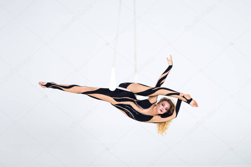 Young woman gymnast wearing black costume on trapeze on white background