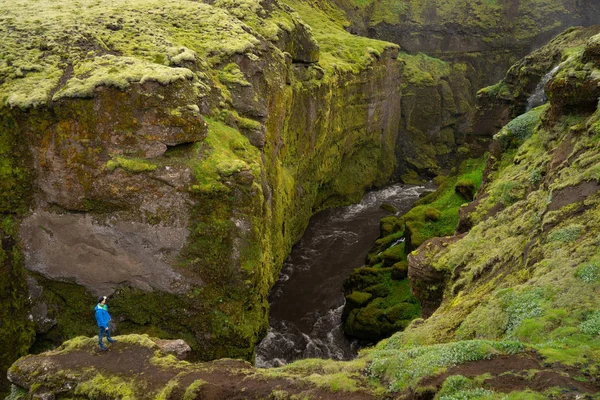 Людина дивиться на прекрасну річку з крихітним водоспадом в Ісландії, оточений зеленою скелею. — стокове фото