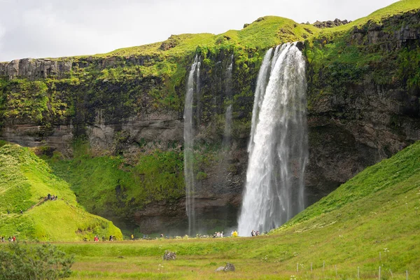 South Region, Iceland - July 29, 2019 - Tourrists visiting the beautiful waterfall of Seljalandsfoss in the summer — стоковое фото
