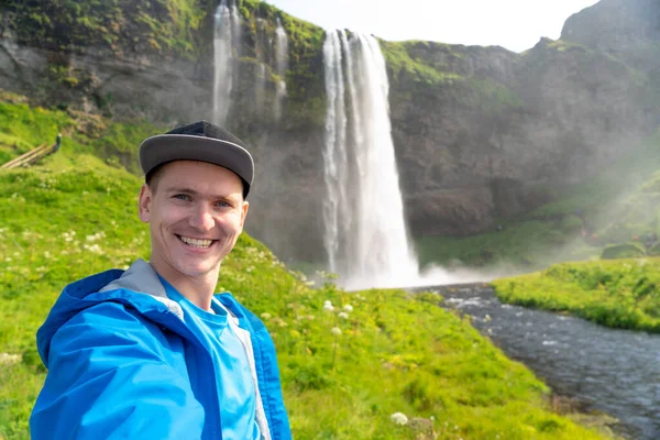 Giovane uomo prendendo selfie con bella cascata di Seljalandsfoss su sfondo. Concetto di viaggiare e stile di vita sano — Foto Stock