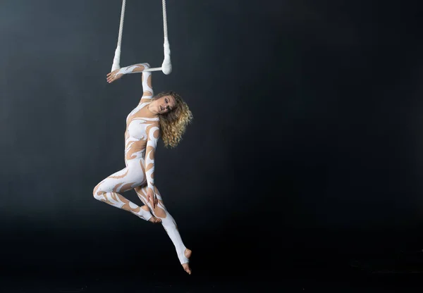 Молода дівчина виконує акробатичні елементи в повітряній трапеції. Студійні зйомки на чорному тлі — стокове фото