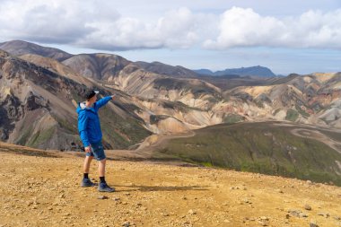 Landmannalaugar Vadisi 'nde sırt çantalı bir yürüyüşçü. İzlanda. Laugavegur yürüyüş yolunda renkli dağlar. Çok renkli kaya, mineral, ot ve yosun katmanlarının birleşimi