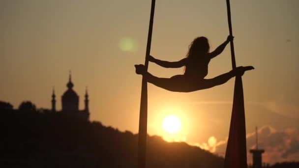 Silueta de una mujer acróbata flexible sobre seda aérea durante una puesta de sol en el fondo de la ciudad de Kiev. concepto de libertad y paz — Vídeos de Stock