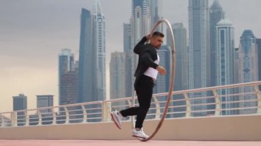 Cyr Wheel sanatçısı yavaş çekimde numaralar yapıyor. Gün batımında Dubai 'nin arka planında siyah beyaz kıyafetler giyiyor.