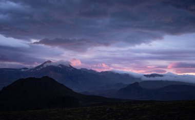 Dramatik ve renkli günbatımında karlı ve bulutlu dağ zirvesi