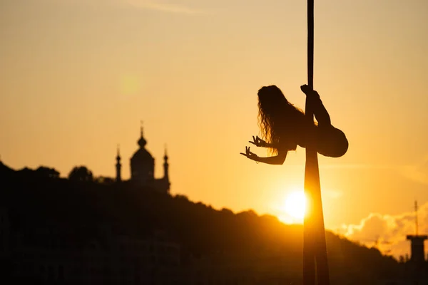 キエフの都市の背景に夕日の間に空中シルクに柔軟な女性の曲芸のシルエット。自由と平和の概念 — ストック写真