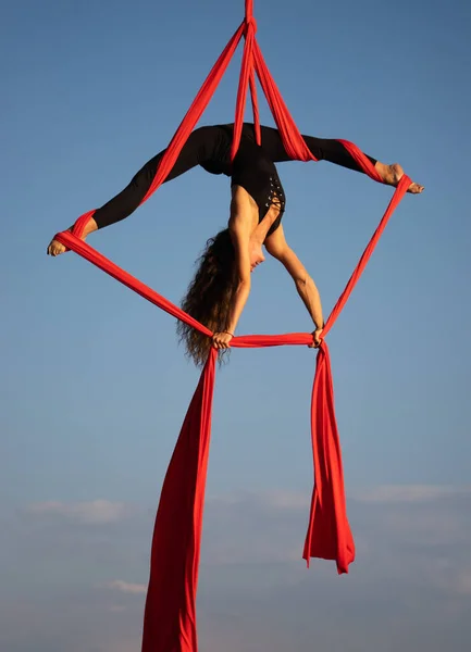 Hermosa y flexible artista de circo femenino bailando con seda aérea sobre un fondo de cielo —  Fotos de Stock