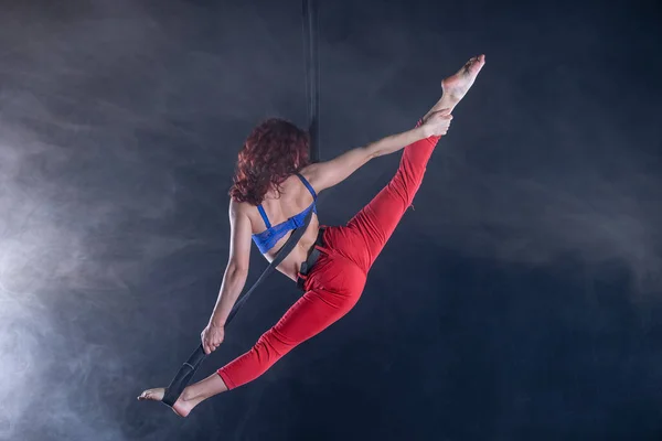 Mujer atlética, sexy y flexible artista de circo aéreo con pelirroja en correas aéreas sobre fondo negro — Foto de Stock